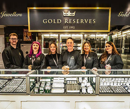 The Gold Reserves team standing behind the jewel counter at Swansea Market, beneath the EST. 1992 crown signage.